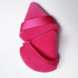Detail of soft pink velvet triangular makeup powder puff with silk ribbon on white background