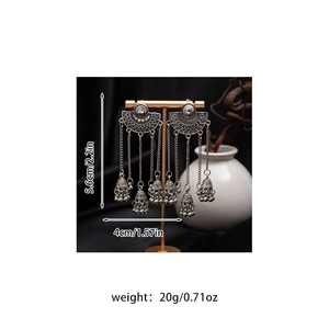 Detail view of vintage silver tassel earrings with size measurements on a golden display stand