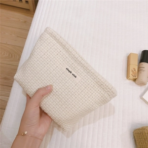 Close-up of hand holding a cream waffle weave makeup bag with simple wish textile label