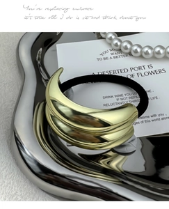 Close-up of sleek gold crescent metal hair tie with polished finish on a silver tray