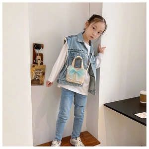 Detail of child wearing blue denim vest with white print and a woven straw crossbody bag
