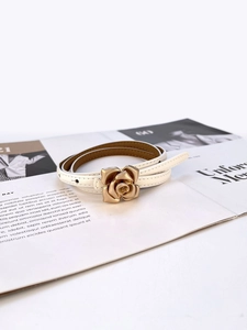 Detail of white leather belt featuring a golden rose flower metal buckle on a magazine