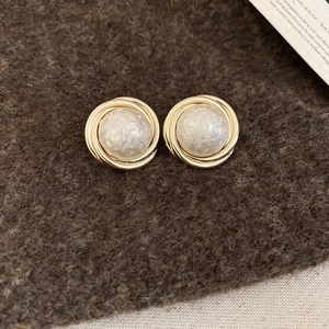 Detailed shot of gold-plated twisted pearl earrings on textured brown wool fabric