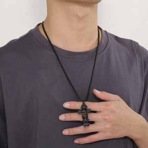 Close-up of a black stainless steel bicycle chain cross pendant on a pearl chain