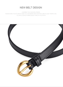 Detail of a thin black leather belt featuring a polished golden round metal buckle