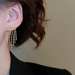 Close-up of golden metallic tassel earring on model showing minimalist design and shine