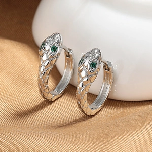 Macro shot of silver snake earrings with green gemstone eyes on elegant silk fabric