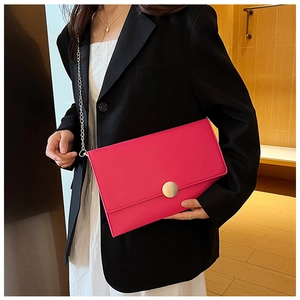 Dettaglio della borsa a busta fucsia con fibbia dorata e catena su un blazer nero