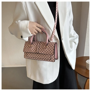 Chic retro patterned crossbody bag with pink leather handles worn by model in white suit