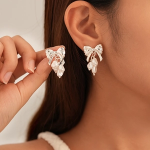 Detail of silver bow earrings with dangling pearls shown on a model for size
