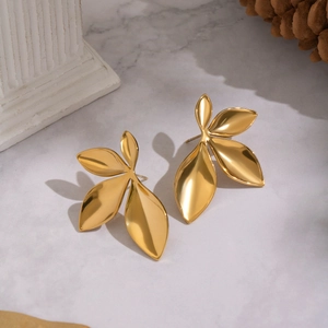 Polished gold petal stud earrings displayed on a marble background with artistic props