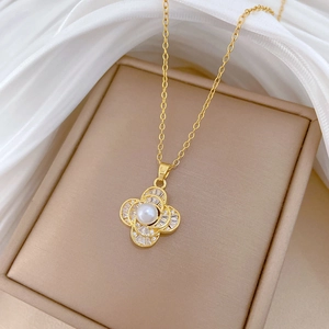 Detailed close-up of a gold necklace with clover pendant, pearl, and cubic zirconia