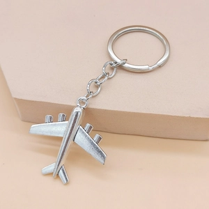 Detailed view of matte silver airplane pendant with metal keyring on pastel background