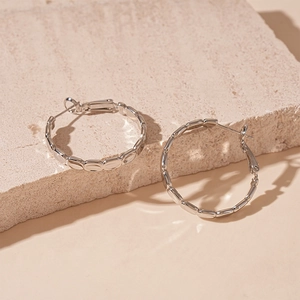 Detail of silver oval hoop earrings with a segmented bamboo-like metallic texture