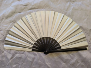 Macro detail of a 33cm silver Kung Fu fan with black bamboo ribs on grey fabric