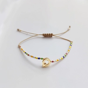 Nahaufnahme des böhmischen Perlenarmbands mit goldenem Q-Anhänger und Kordelzug