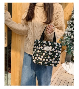 Close-up of a small black canvas handbag with white daisy prints and woven handles