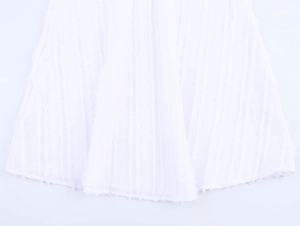 Detail of white dress hem featuring vertical textured stripes and fringe edging