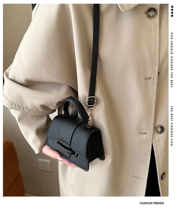Detail of black mini handbag with lychee texture and curved base shown on model