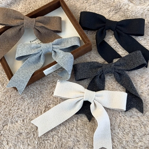 Knitted bow hair clips in five earthy colors on a soft plush background and wooden tray