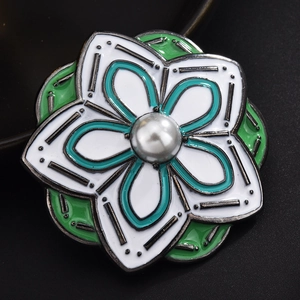 Close-up of white and green enamel flower brooch with center pearl and golden edges