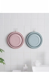 Space-saving foldable plastic washbasins in pink and blue hanging on a bathroom wall hook