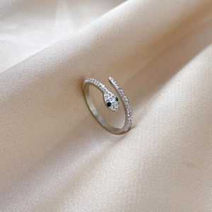 Detailed view of silver snake ring with white crystals and green eyes on silk