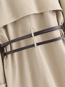 Dettaglio del retro del trench con mantellina e cinture in pelle marrone scuro in vita
