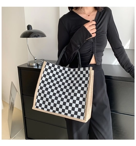 Detail of checkered canvas tote bag with woven straw edges held by model in modern room