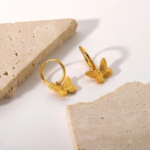 Detailed view of 18K gold plated butterfly drop earrings on textured stone base