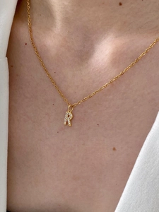 Close-up of a gold-plated letter R pendant necklace with zircon pavé on a female neck