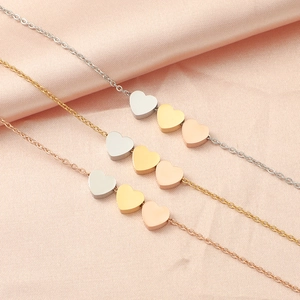 Minimalist heart charm necklaces in silver, gold, and rose gold on pink satin background