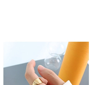 Nahaufnahme eines Goldrings mit Wellendesign, getragen von einem Modell vor grauem Hintergrund