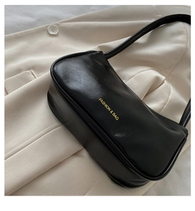 Detail of black underarm bag with glossy leather texture and gold FASHION & BAG lettering