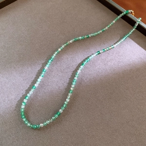 Detailed close-up of emerald green faceted crystal beaded necklace on a grey velvet background