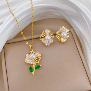 Elegant gold flower jewelry set with pearls and green leaves on white fabric background