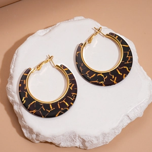 Detailed view of large gold and black resin hoop earrings on a white stone base