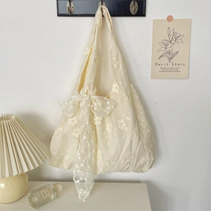 Detail of floral embroidery on a cream lace tote bag with a decorative bow accent