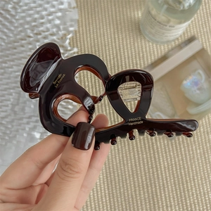 Deep brown acetate hair claw clip with gold lettering on a soft textured background