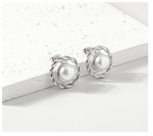Macro shot of silver twisted metal stud earrings with central white pearl on a stone base