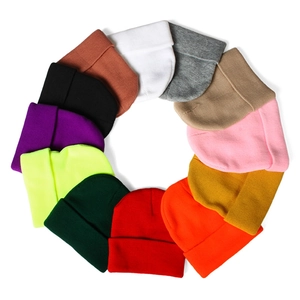 Flat lay of twelve colorful knitted beanies arranged in a circle on a white background
