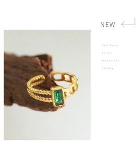 Macro shot of gold-tone titanium ring featuring a green zircon and dual-layer chain band
