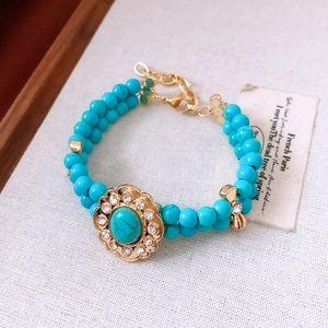 Dettaglio del bracciale a doppio strato in turchese con ciondolo a fiore dorato e orso