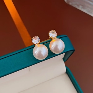 Gros plan de boucles d'oreilles perles dorées avec zircons dans un écrin vert foncé