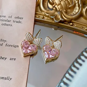 Gold-plated bow earrings with pink heart zircon and pearls on a mirror surface