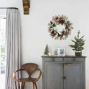 Close-up of Christmas wreath with red berries, pine cones and frosted leaves on white wall