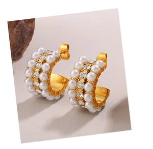 Close-up of gold C-shape earrings with inlaid white pearls and sparkling crystals