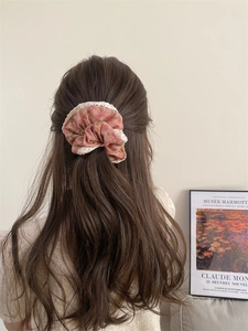 Pink floral corduroy scrunchie with white lace trim worn by woman in soft light