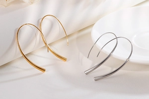 Minimalist gold and silver long hook earrings displayed on elegant white fabric