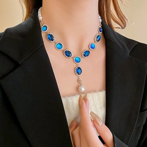 Dettaglio della collana di perle e gemme ovali blu su modella con abito nero elegante